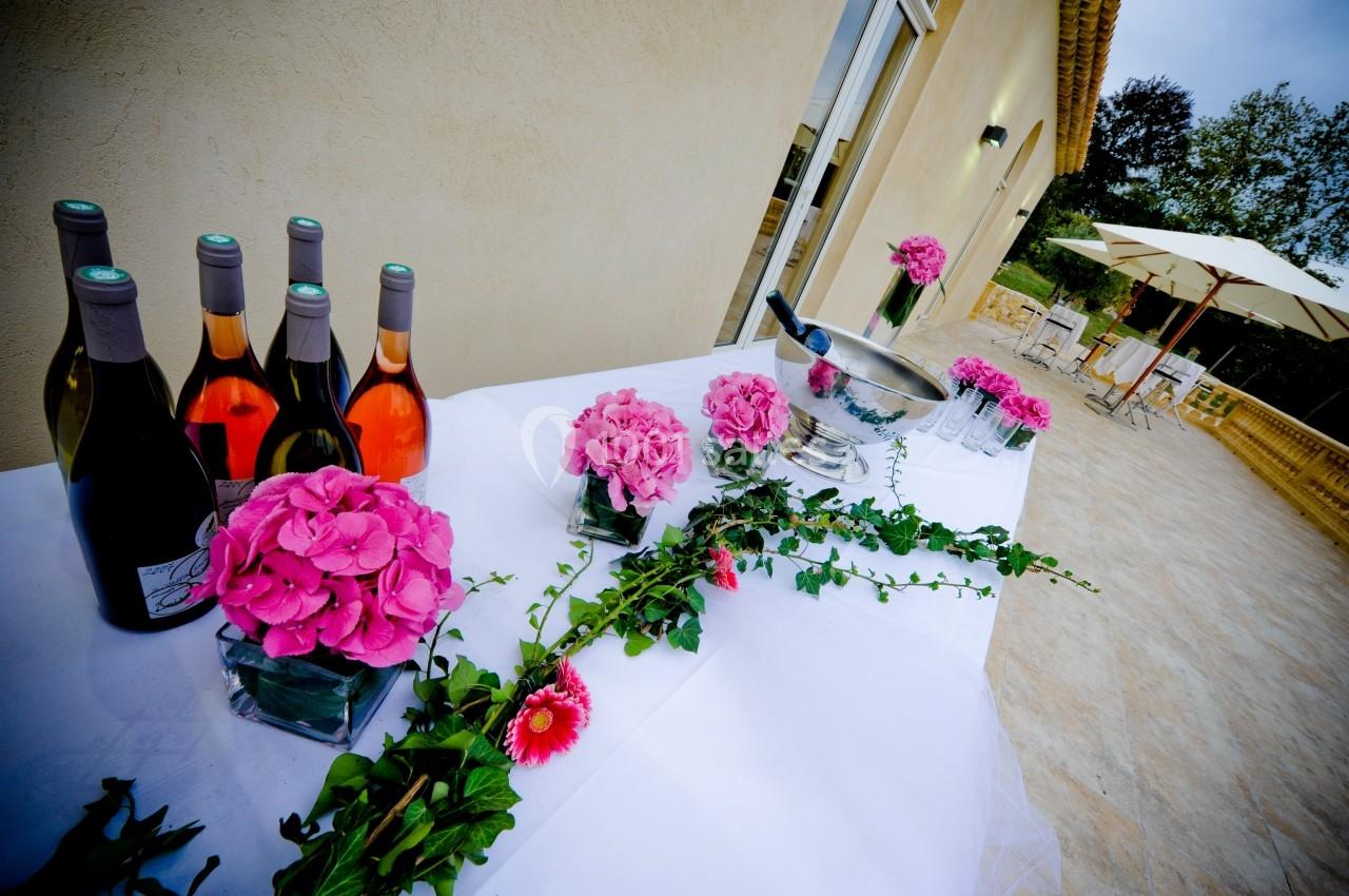 Bouteilles de vin, fleurs roses et seau à champagne disposés sur une table blanche en extérieur.