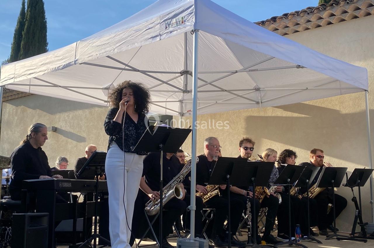 Une chanteuse interprète sur scène avec un groupe de musiciens sous une tente blanche en extérieur.