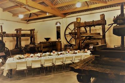 Salle avec de grandes presses anciennes en bois et une longue table dressée pour un repas.