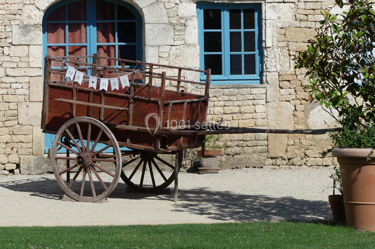 Location salle Sainte-Gemme-la-Plaine (Vendée) - Château de la Chevallerie #25 Charrette en bois ancienne avec des roues en métal, décorée d'une guirlande, devant un bâtiment en pierre.