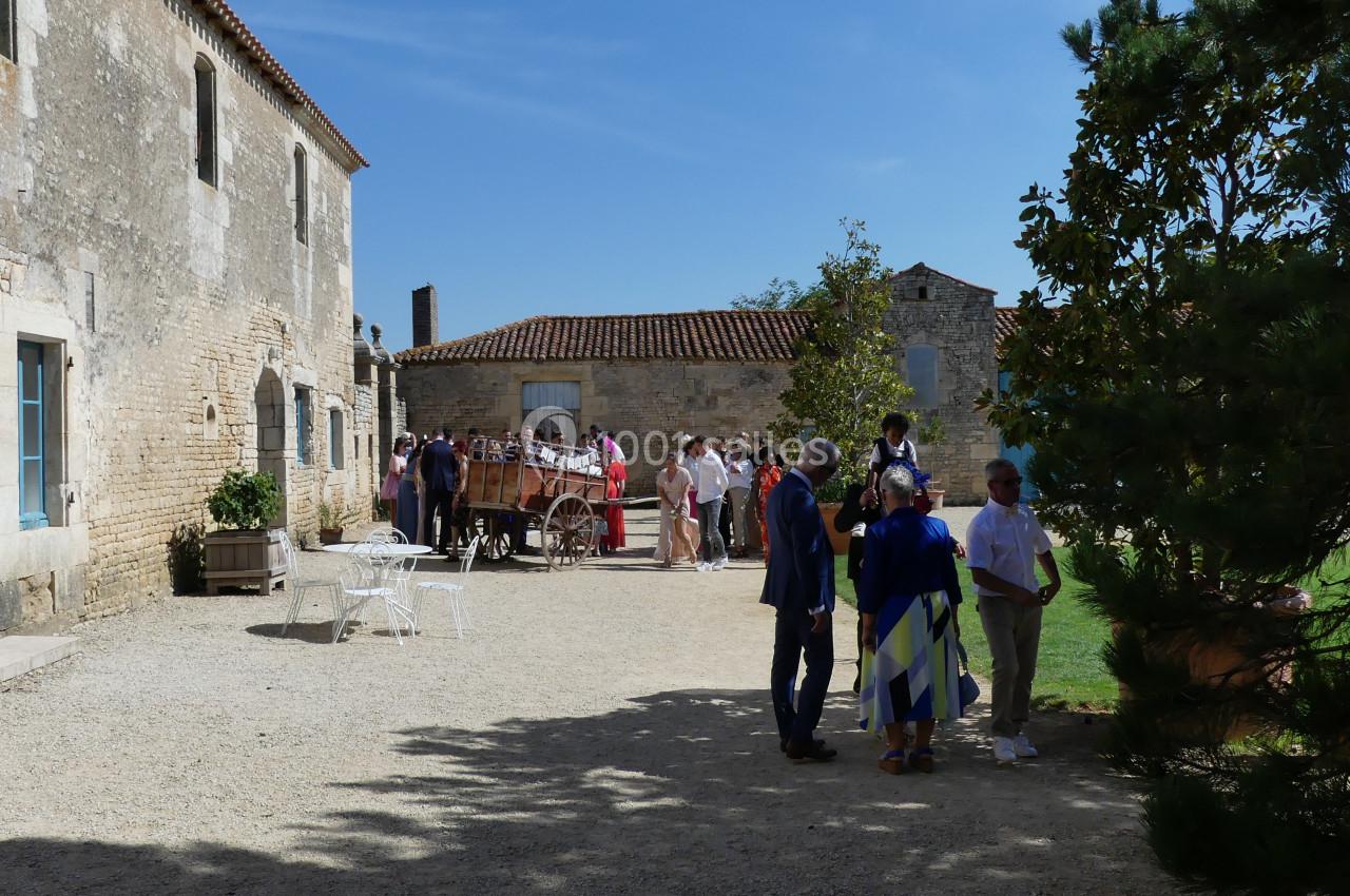 Location salle Sainte-Gemme-la-Plaine (Vendée) - Château de la Chevallerie #13 Groupe de personnes discutant dans une cour ensoleillée entourée de bâtiments en pierre et d'arbres.
