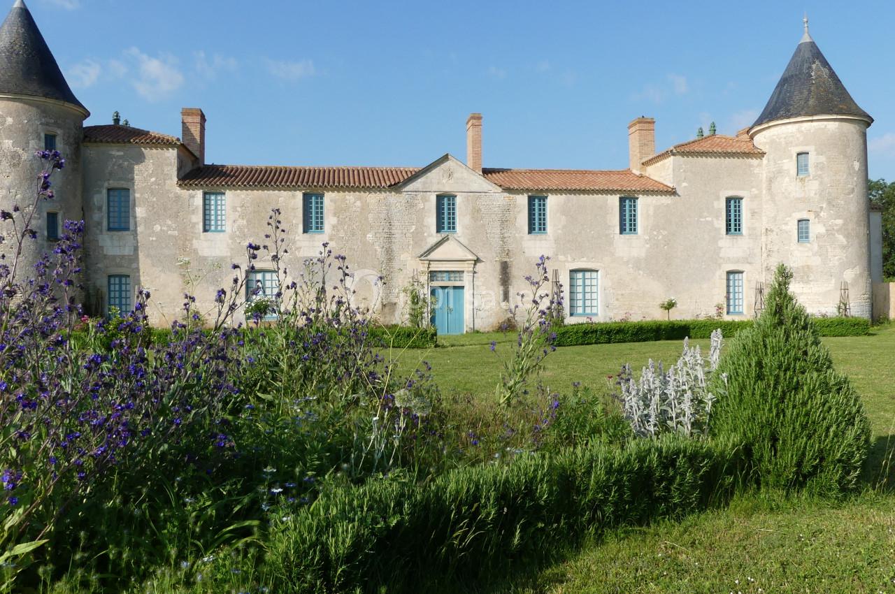 Location salle Sainte-Gemme-la-Plaine (Vendée) - Château de la Chevallerie #27 Façade d'un château ancien avec deux tours rondes, entouré de jardins fleuris et d'une pelouse verte.