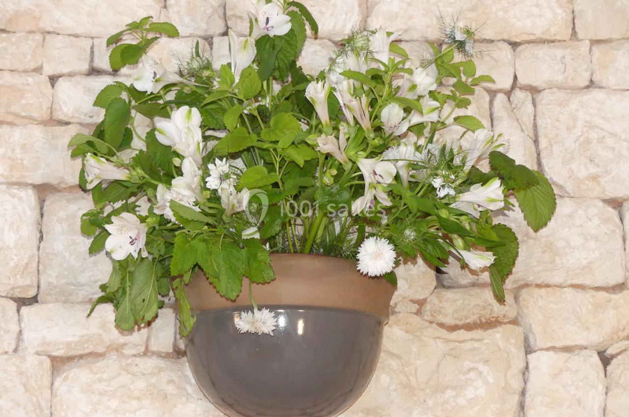 Location salle Sainte-Gemme-la-Plaine (Vendée) - Château de la Chevallerie #30 Pot mural en céramique contenant un bouquet de fleurs blanches et de feuillage vert, fixé sur un mur en pierre beige.