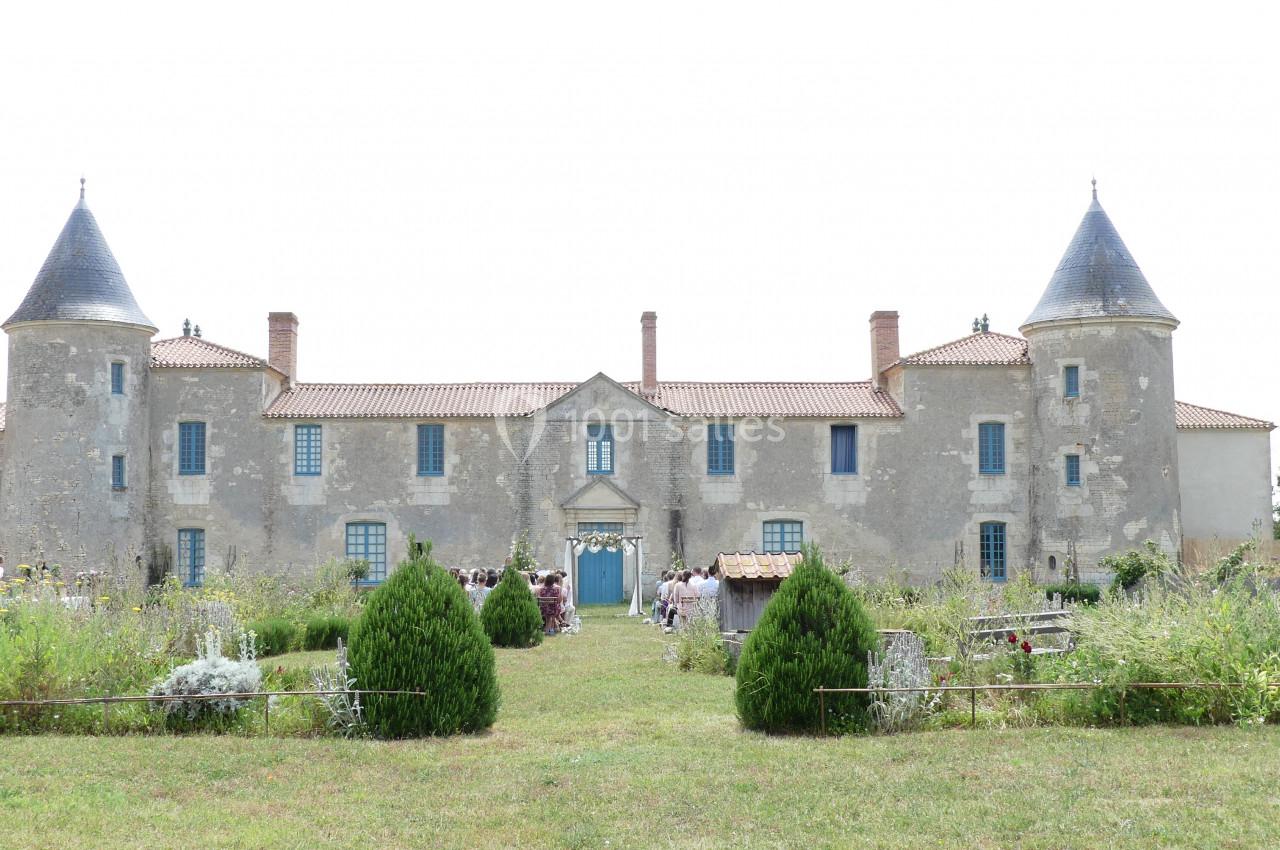 Location salle Sainte-Gemme-la-Plaine (Vendée) - Château de la Chevallerie #31 Façade d'un château ancien avec deux tours, entouré de jardins verdoyants et d'arbustes.