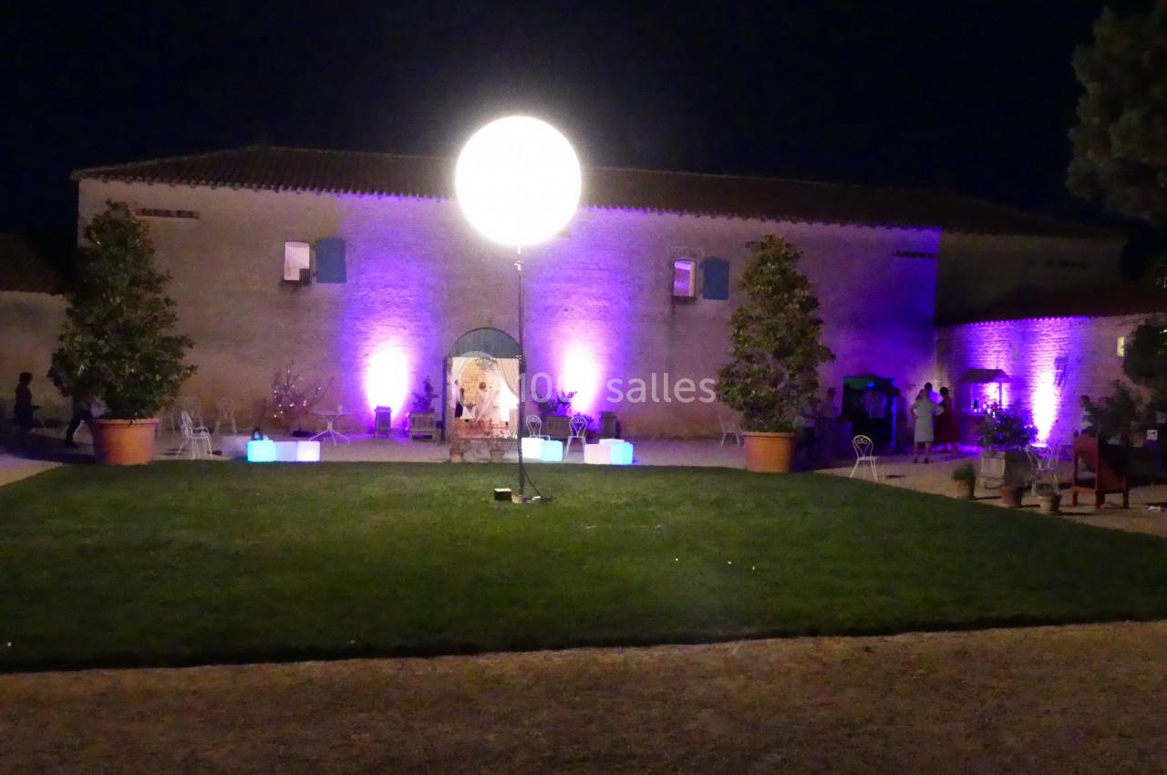 Location salle Sainte-Gemme-la-Plaine (Vendée) - Château de la Chevallerie #36 Cour extérieure éclairée la nuit avec un grand ballon lumineux central, des murs en pierre et des lumières colorées.