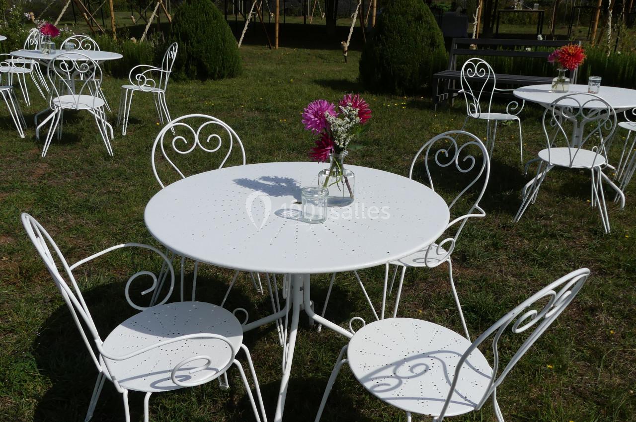 Location salle Sainte-Gemme-la-Plaine (Vendée) - Château de la Chevallerie #39 Tables et chaises en fer forgé blanc disposées sur une pelouse, avec des bouquets de fleurs au centre des tables.