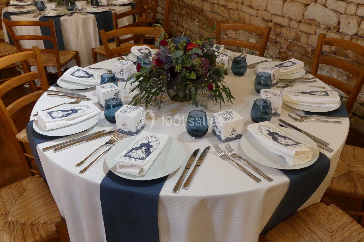 Location salle Sainte-Gemme-la-Plaine (Vendée) - Château de la Chevallerie #19 Table dressée avec nappes blanches et chemins de table bleus, ornée d'un centre de table floral et de couverts disposés.