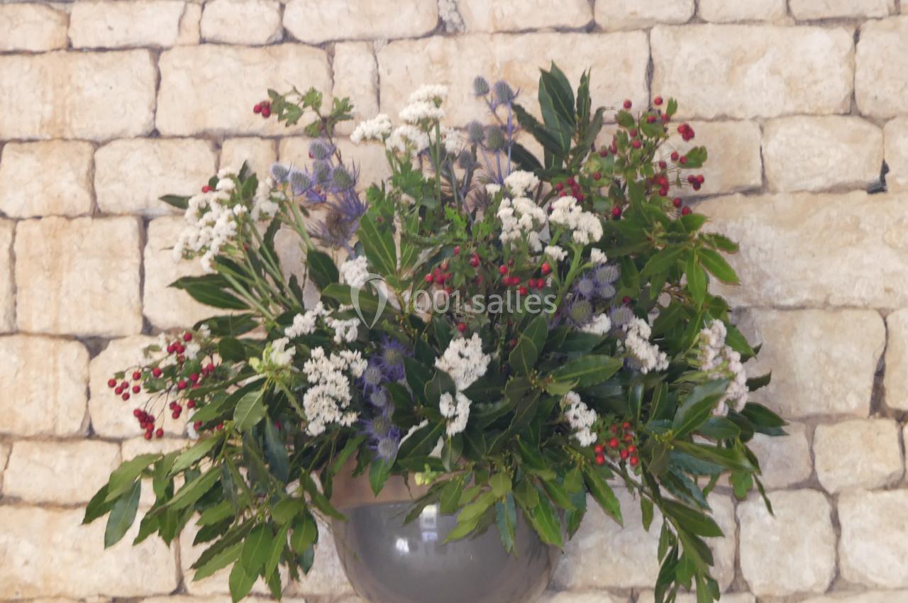 Location salle Sainte-Gemme-la-Plaine (Vendée) - Château de la Chevallerie #23 Arrangement floral coloré avec des fleurs blanches, rouges et violettes, suspendu devant un mur en pierre beige.