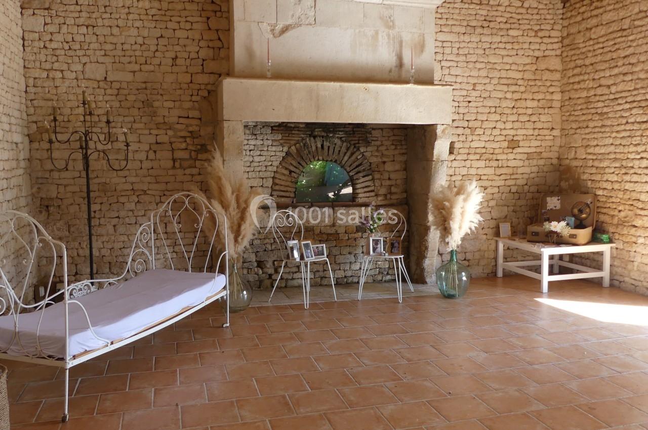 Location salle Sainte-Gemme-la-Plaine (Vendée) - Château de la Chevallerie #34 Salle en pierre avec cheminée ancienne, canapé en fer forgé, décorations végétales et lumière naturelle.