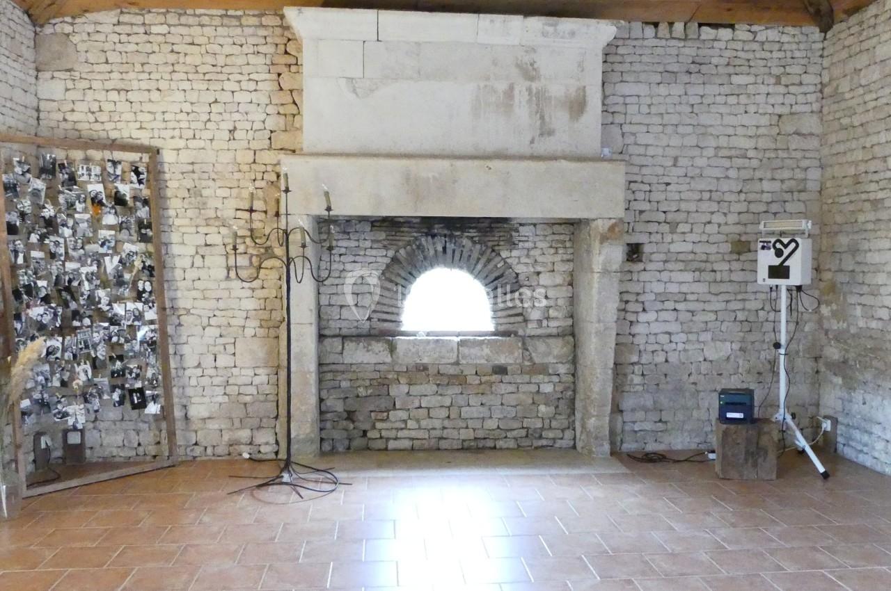 Location salle Sainte-Gemme-la-Plaine (Vendée) - Château de la Chevallerie #33 Salle en pierre avec cheminée ancienne, mur décoré de photos en noir et blanc et équipement technique à droite.