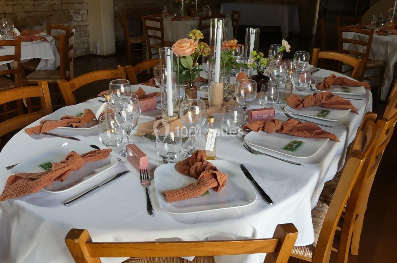Location salle Sainte-Gemme-la-Plaine (Vendée) - Château de la Chevallerie #10 Table dressée avec nappes blanches, serviettes orange, verres, couverts et décorations florales dans un cadre chaleureux.