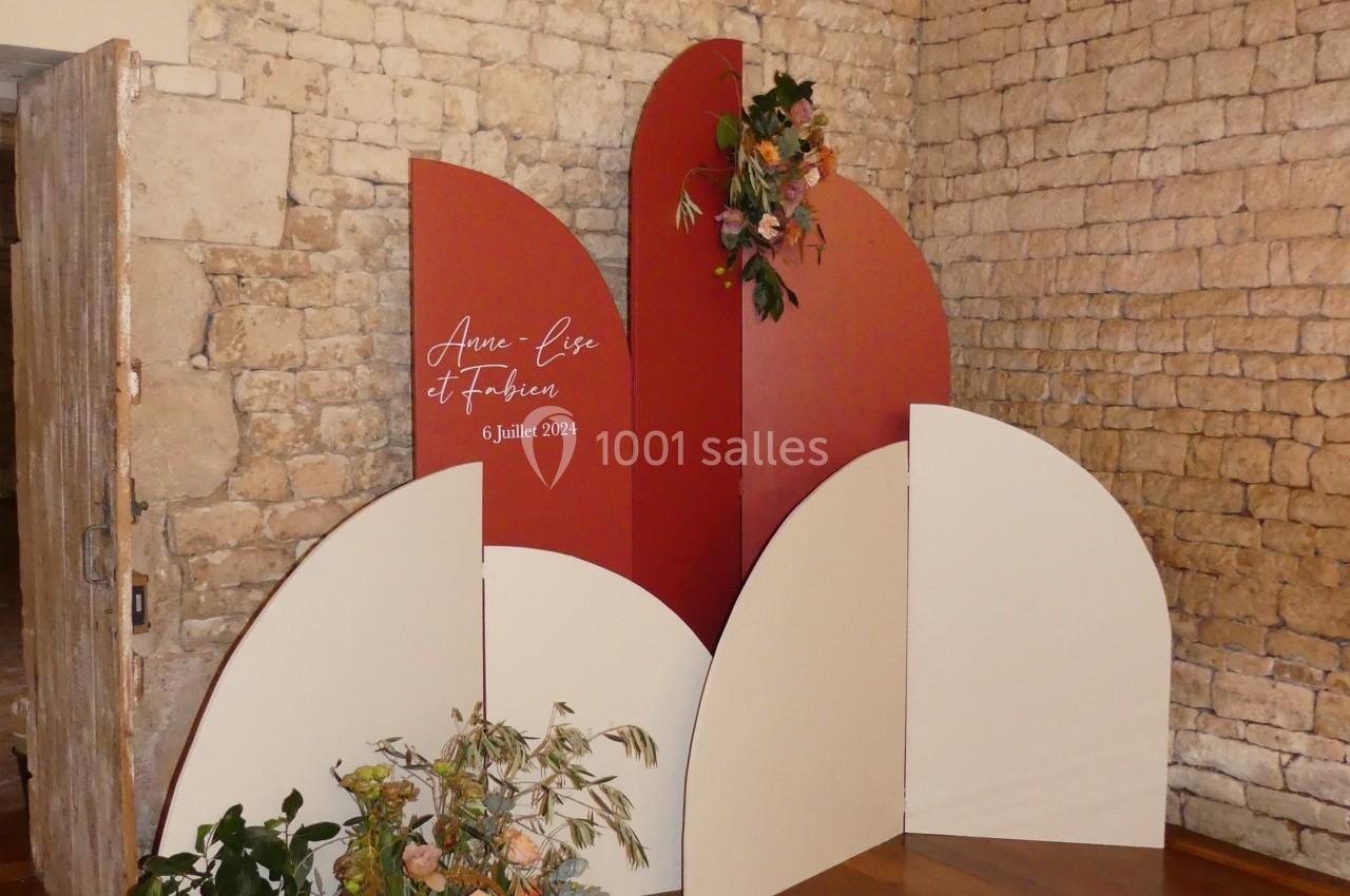 Location salle Sainte-Gemme-la-Plaine (Vendée) - Château de la Chevallerie #49 Mur décoratif en panneaux rouges et blancs avec des fleurs, installé dans une pièce aux murs en pierre.