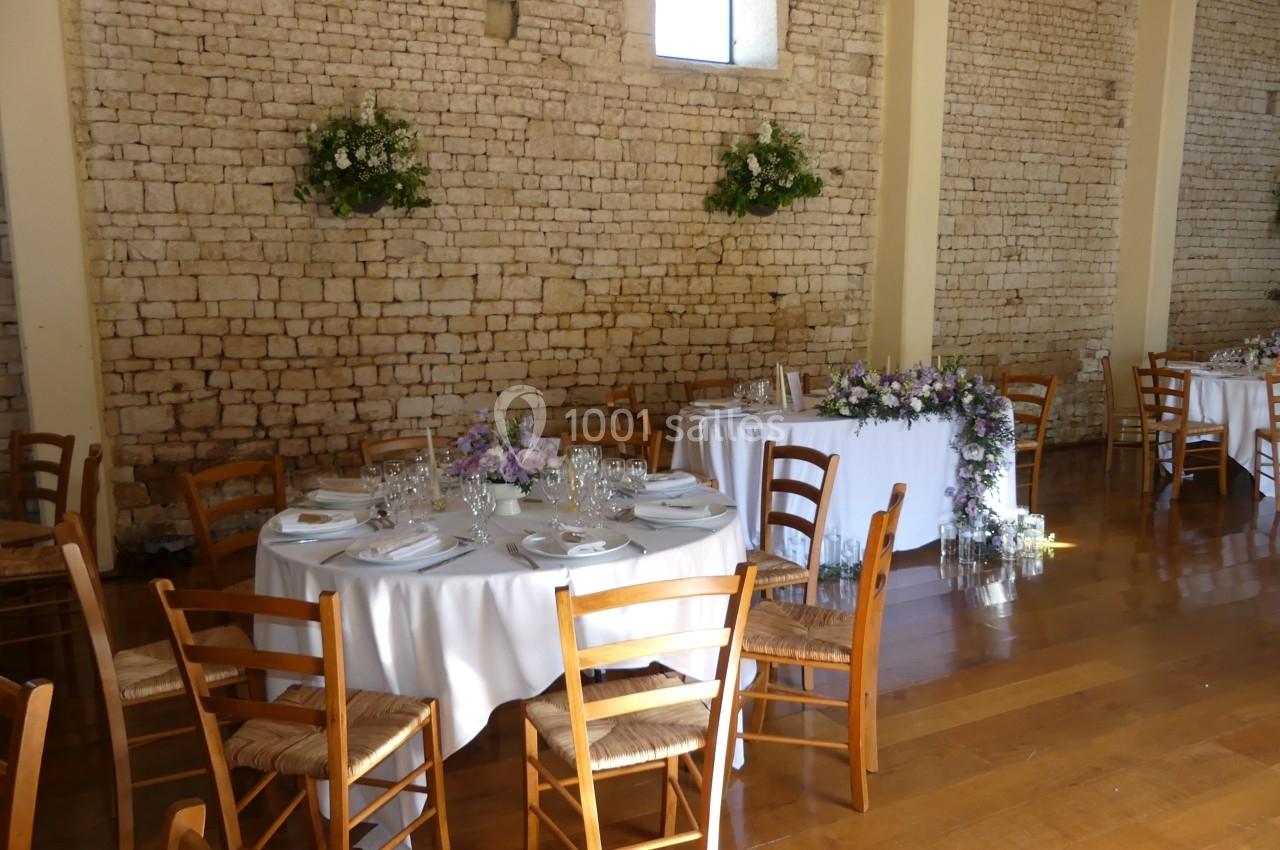 Location salle Sainte-Gemme-la-Plaine (Vendée) - Château de la Chevallerie #11 Salle de réception avec murs en pierre, tables rondes dressées, chaises en bois et décorations florales.