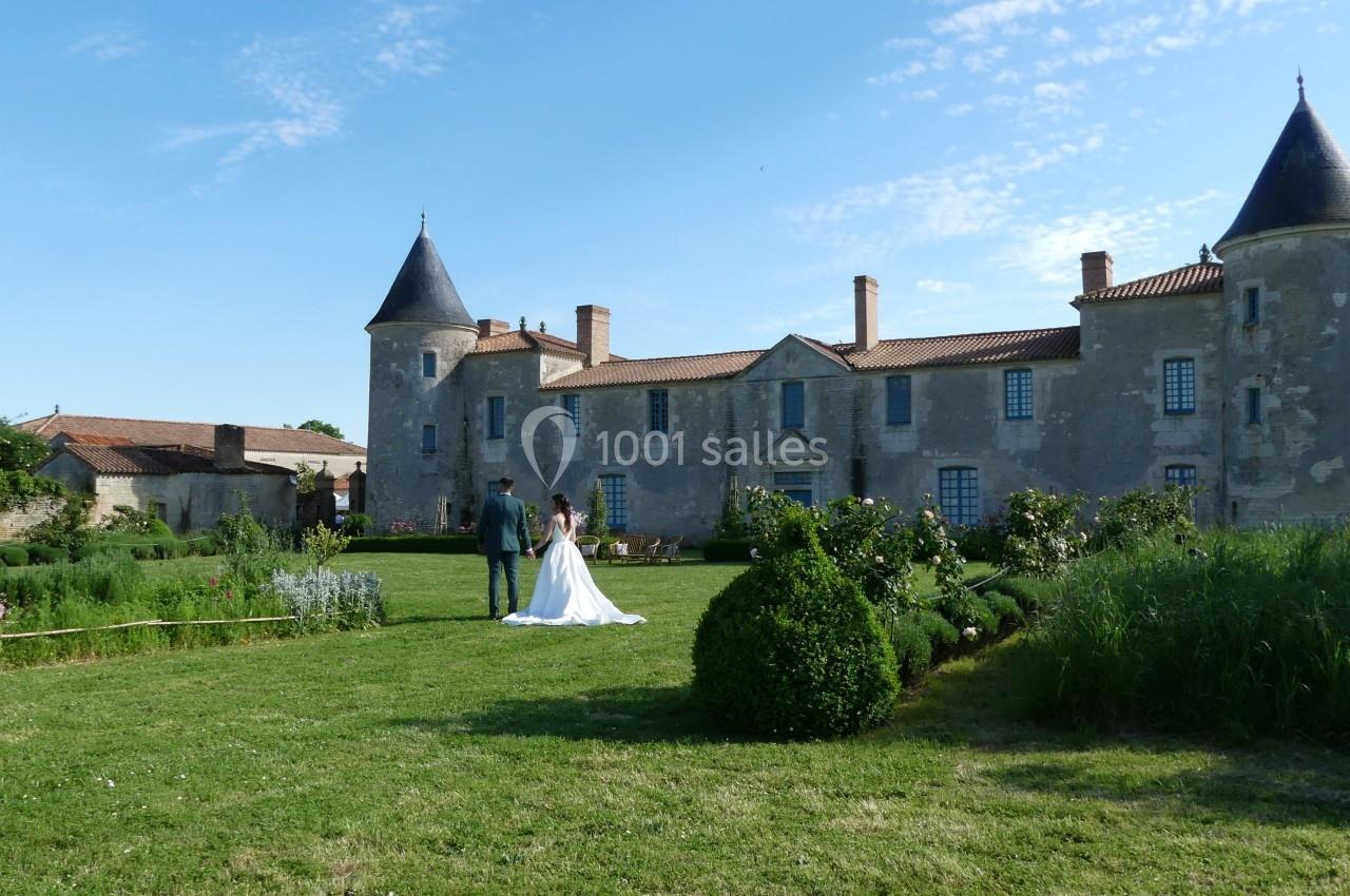 Location salle Sainte-Gemme-la-Plaine (Vendée) - Château de la Chevallerie #50 Un couple marche dans le jardin d'un château ancien entouré de verdure par une journée ensoleillée.