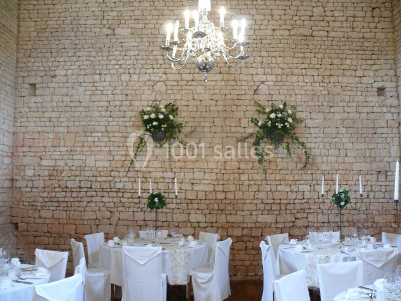 8 bouquets de fleurs produite sur place Salle de réception avec murs en pierre, tables dressées avec nappes blanches et chandelier suspendu.