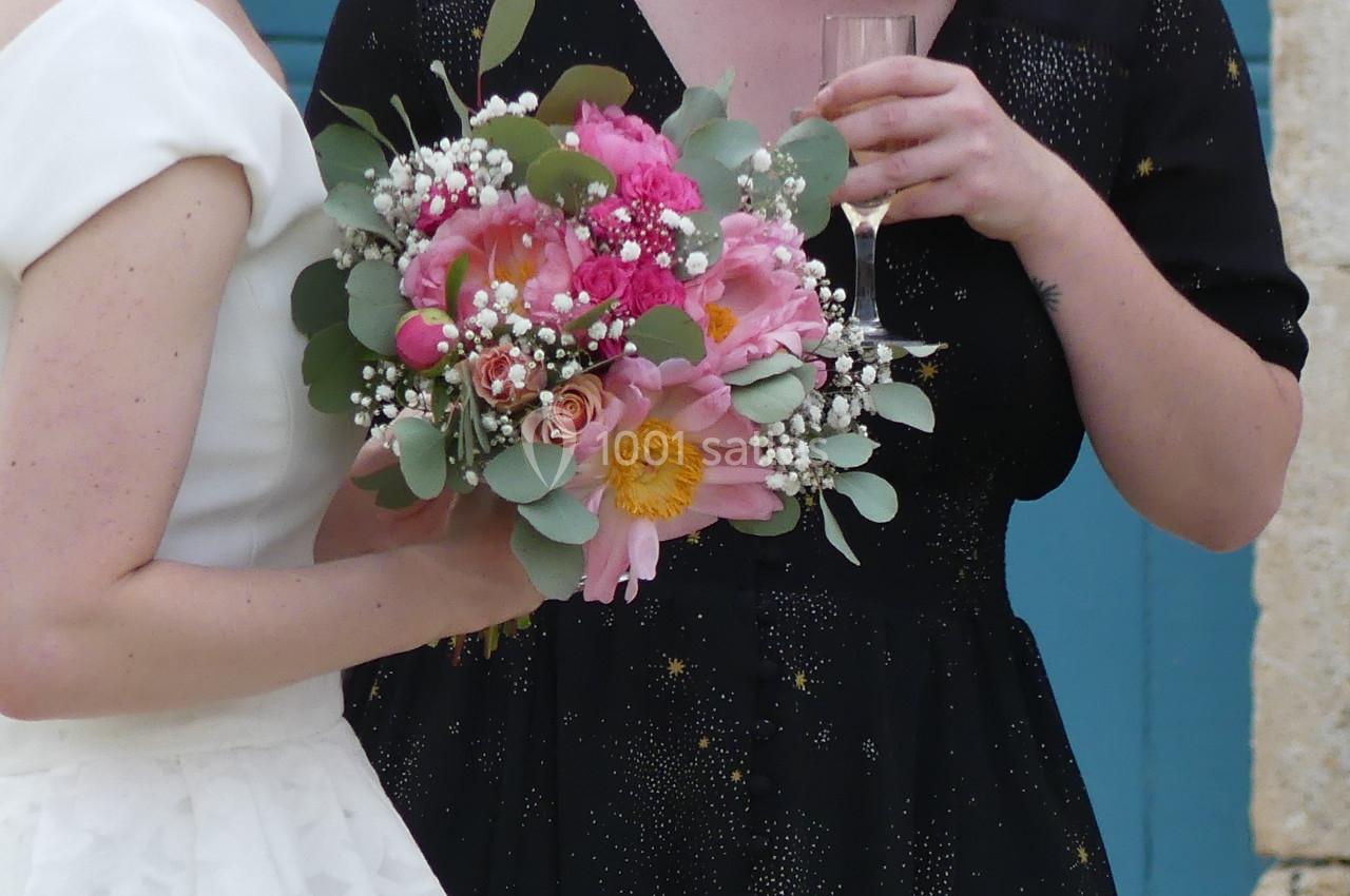 bouquet coloré Deux femmes, l'une en robe blanche tenant un bouquet de fleurs colorées, discutent devant une porte bleue.