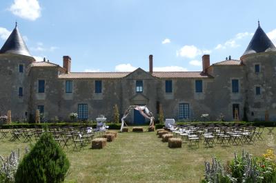 Miniature Cérémonie devant le Château de la Chevallerie Un couple marche dans le jardin d'un château ancien entouré de verdure par une journée ensoleillée.