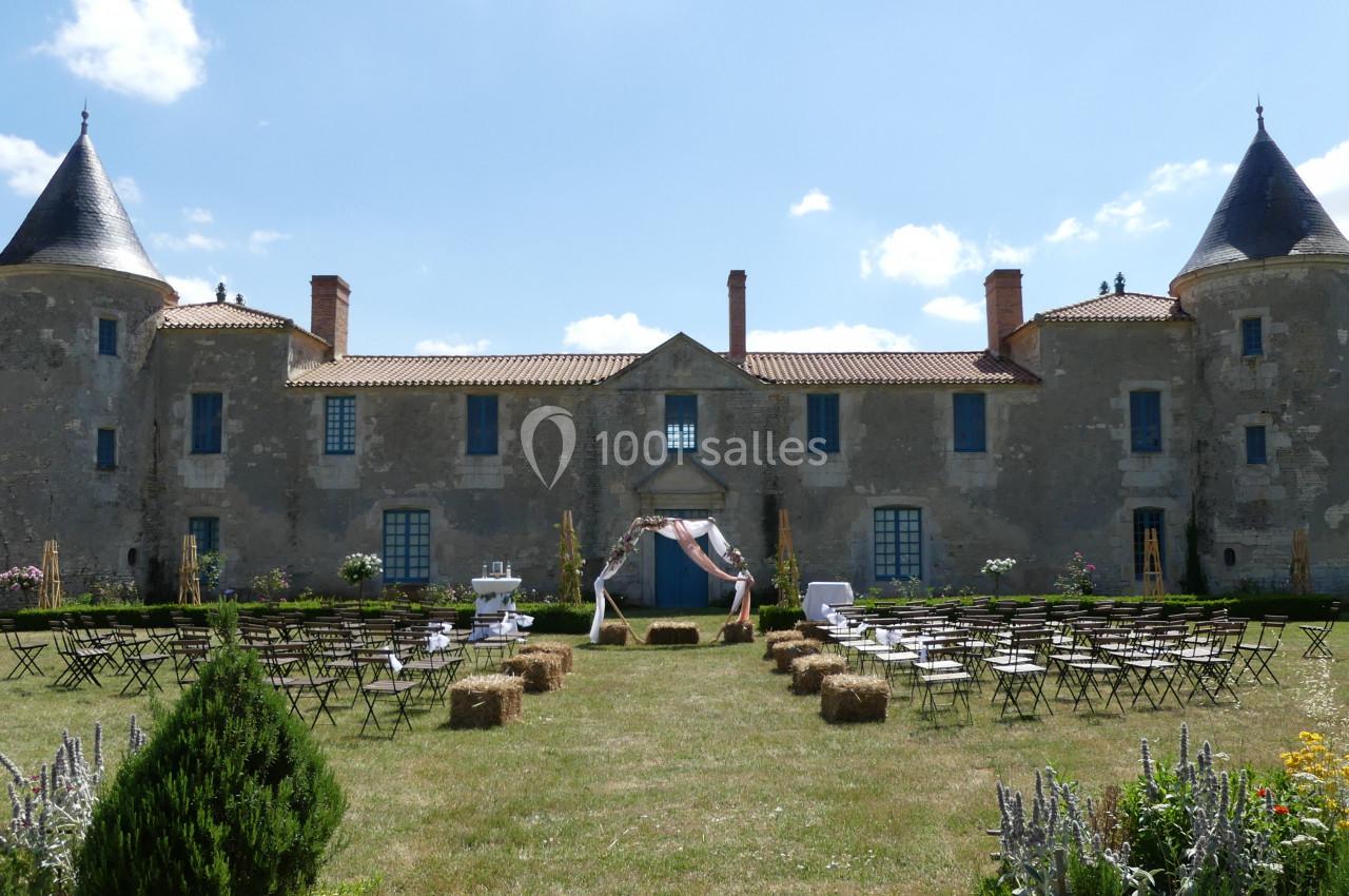 Cérémonie devant le Château de la Chevallerie Façade d'un château en pierre avec une cérémonie en plein air, des chaises et des bottes de paille disposées sur la pelouse.