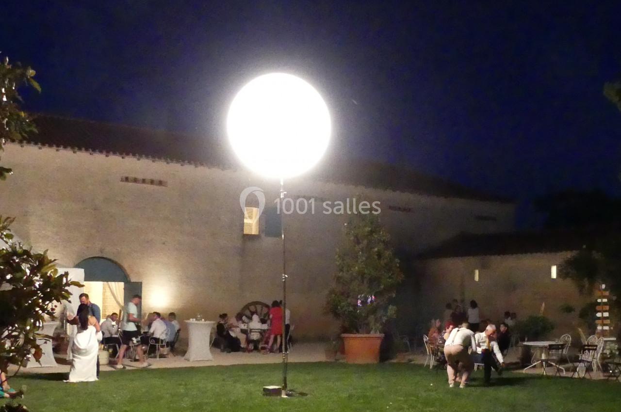 clair de lune Groupe de personnes assises et debout dans une cour extérieure éclairée par une grande lampe ronde, de nuit.