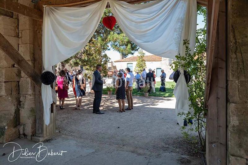 Cour du Pavillon Des invités discutent dans une cour extérieure ensoleillée, vue à travers une arche décorée de rideaux blancs.