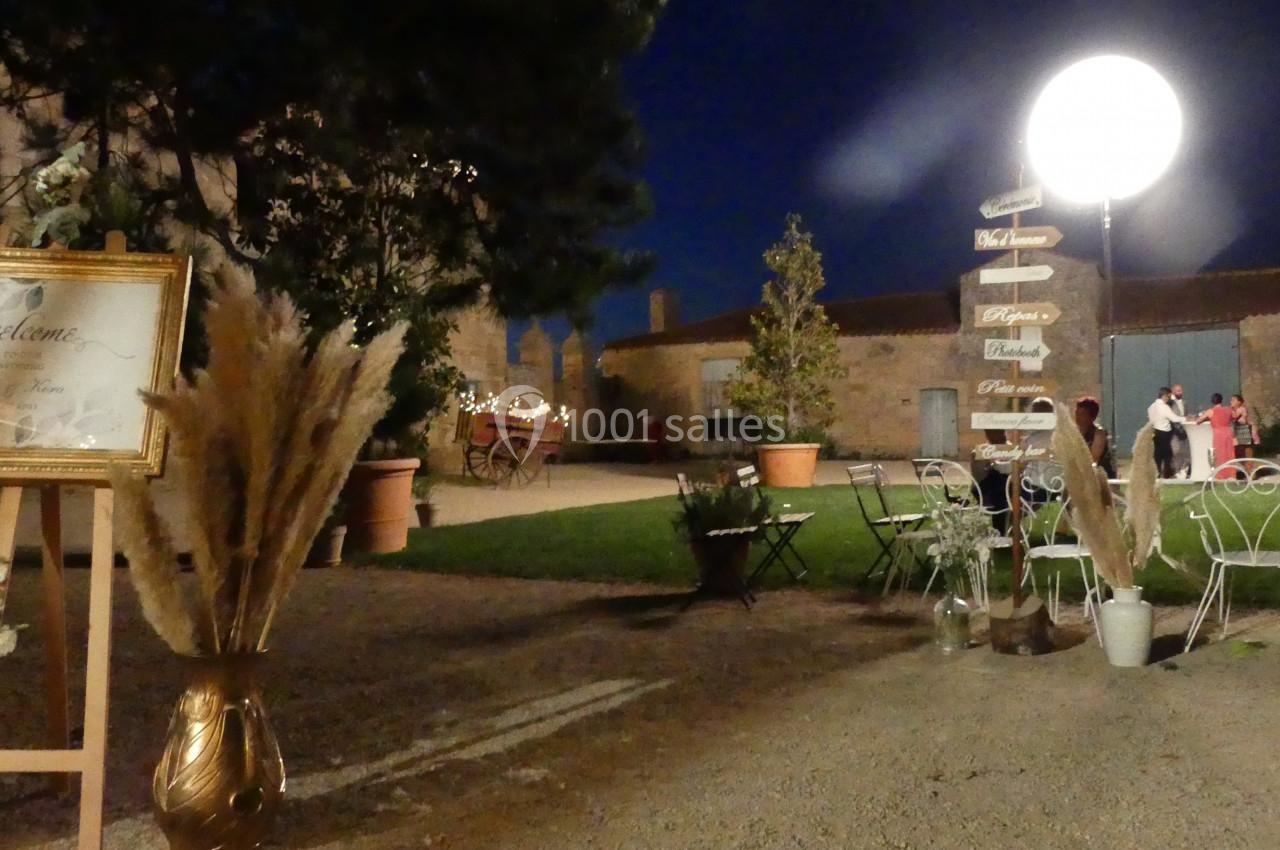 de nuit Espace extérieur éclairé de nuit avec des tables, des chaises, des décorations végétales et un panneau directionnel.