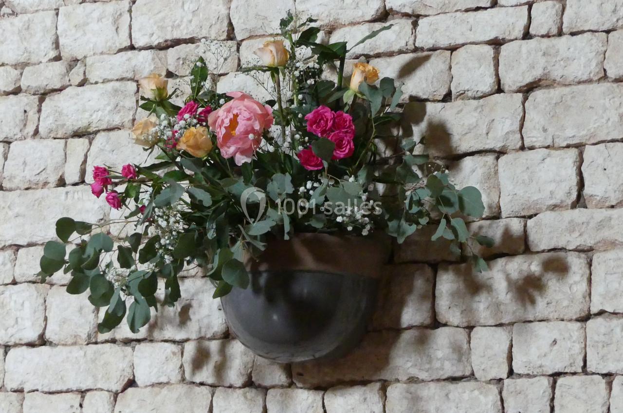 Des fleurs même aux murs ! Bouquet de fleurs colorées dans un vase mural en métal, fixé sur un mur en pierre apparente.