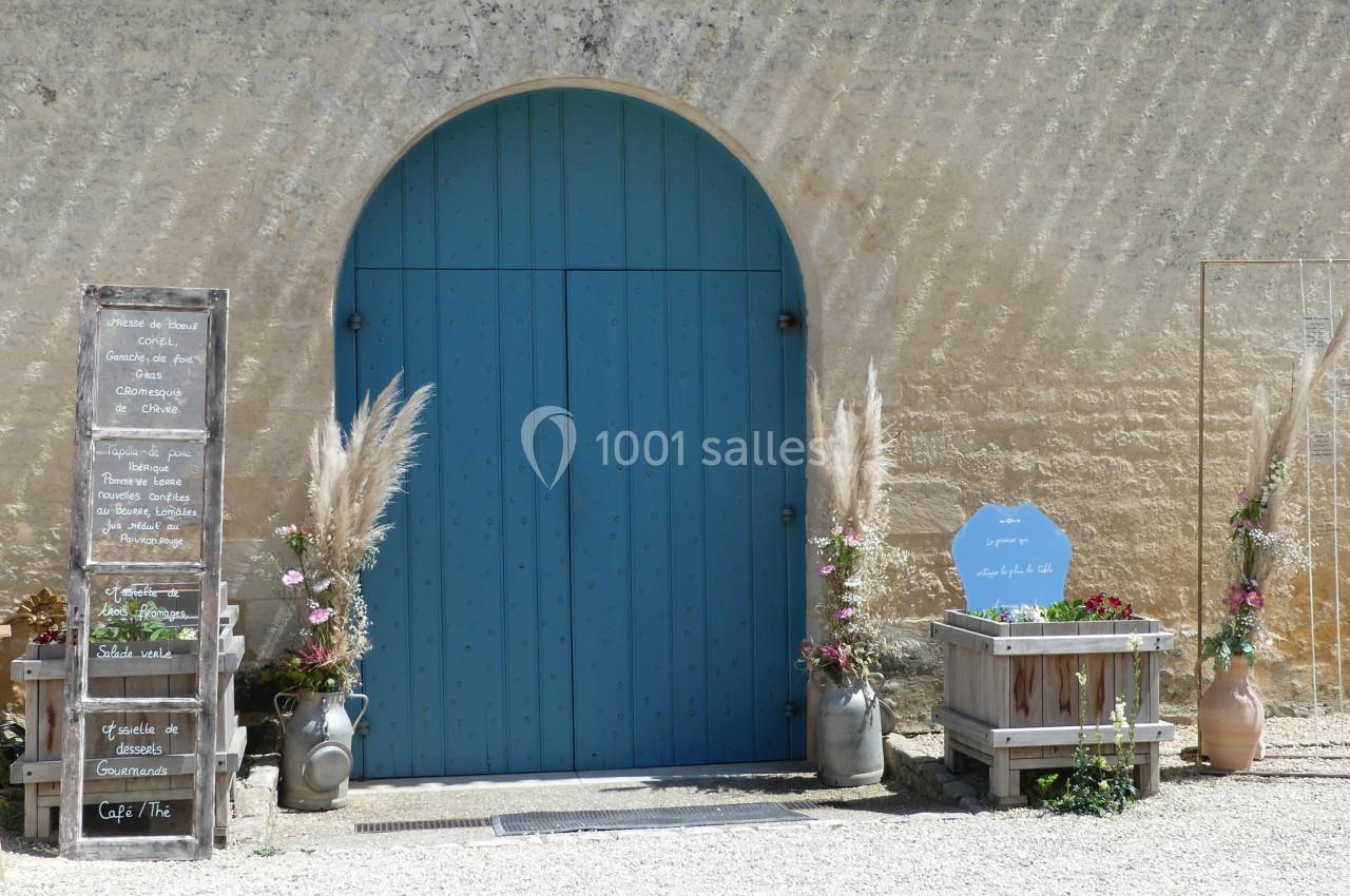Entrée de la Grande Nef Porte bleue arrondie encadrée de décorations florales et panneaux en bois devant un mur en pierre clair.