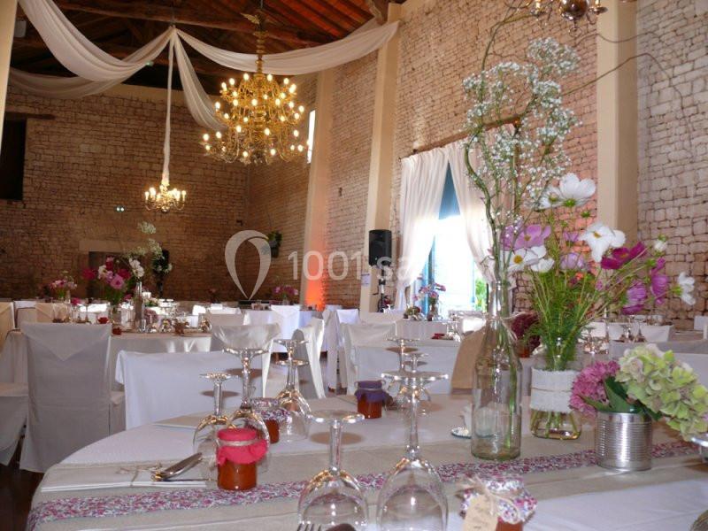 fleurs des champs Salle de réception décorée avec des fleurs, nappes blanches et lustres suspendus sous un plafond en bois.