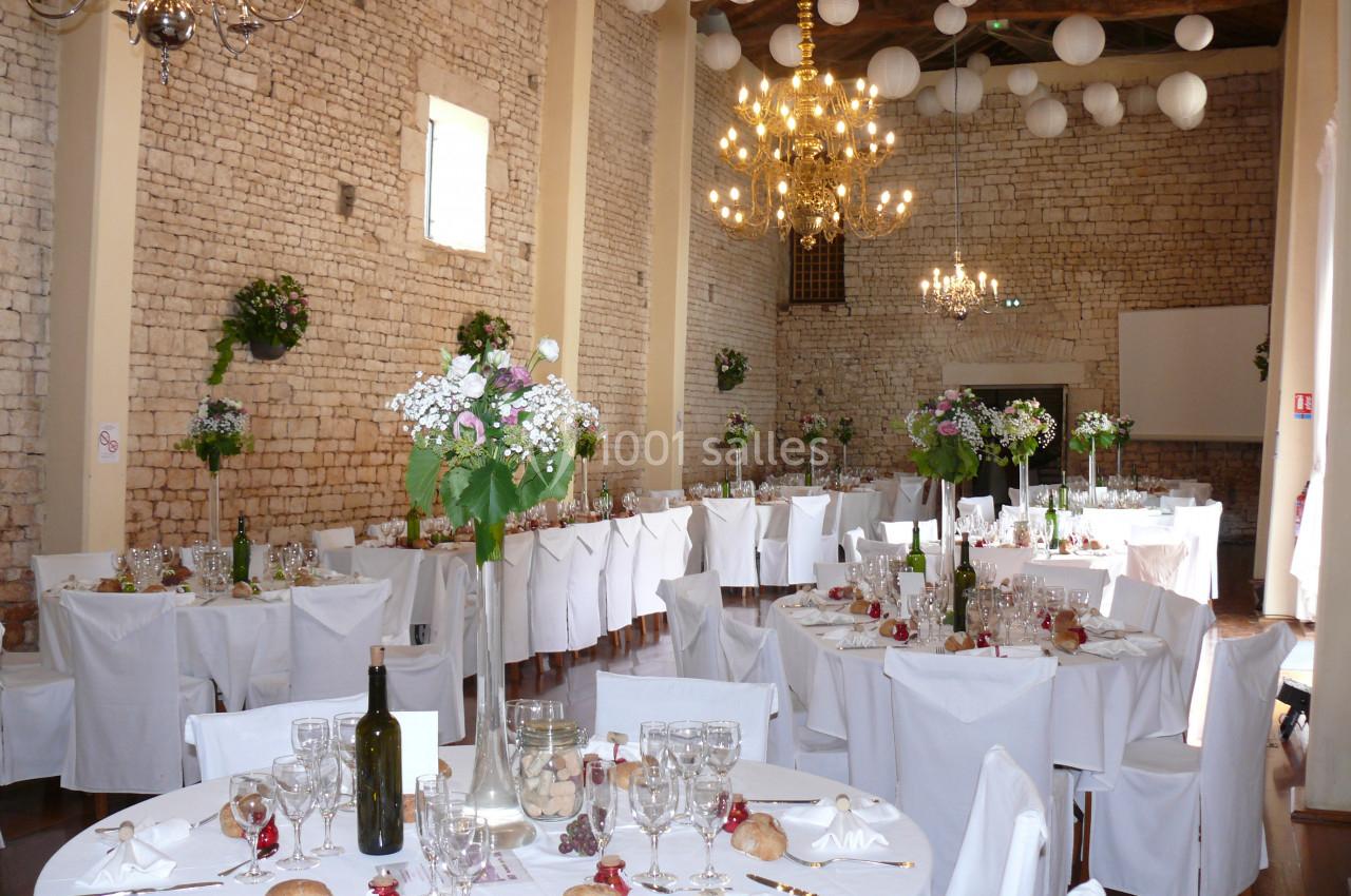 Grande Nef : 150 personnes à table Salle de réception décorée avec des tables rondes dressées, des chaises blanches et des fleurs suspendues.