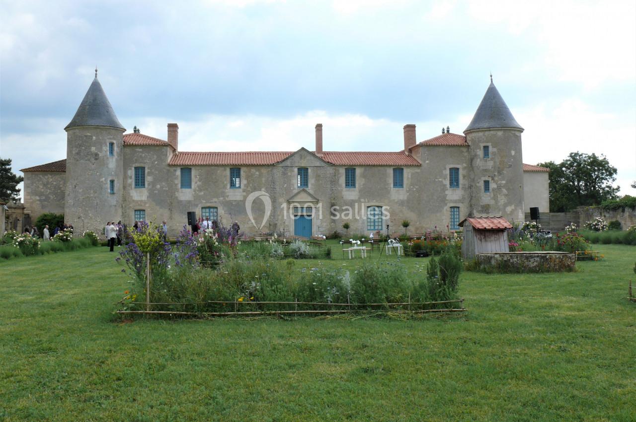 Jardin et vue sur le Château Façade d'un château en pierre avec deux tours, entouré d'un jardin fleuri et d'une pelouse verte.