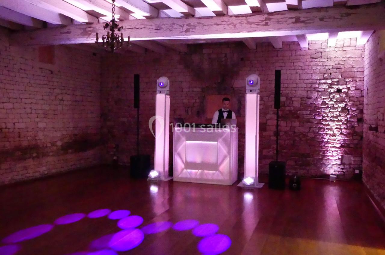 Le Dj est installé Un DJ derrière une table lumineuse dans une salle en pierre avec éclairage violet et parquet en bois.