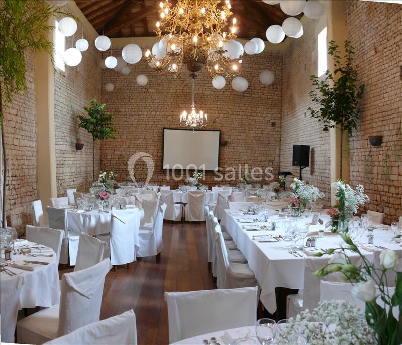 Les décors que vous souhaitez Salle de réception en pierre avec tables dressées, chaises blanches, décorations florales et lustres suspendus.