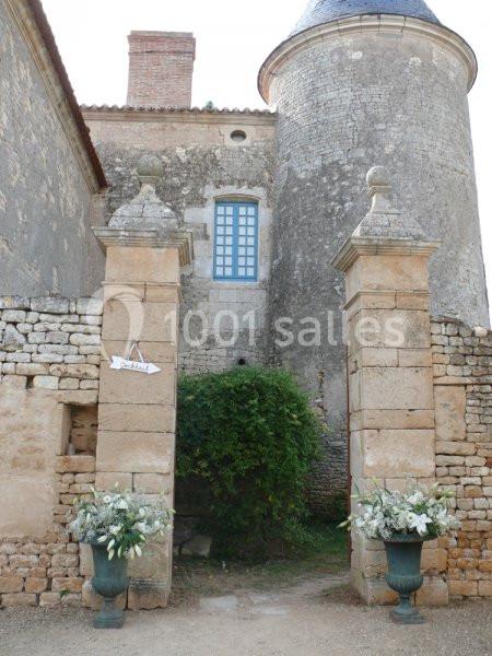Portail du jardin Entrée en pierre d'un bâtiment ancien avec deux piliers décorés de fleurs blanches et une tour en arrière-plan.