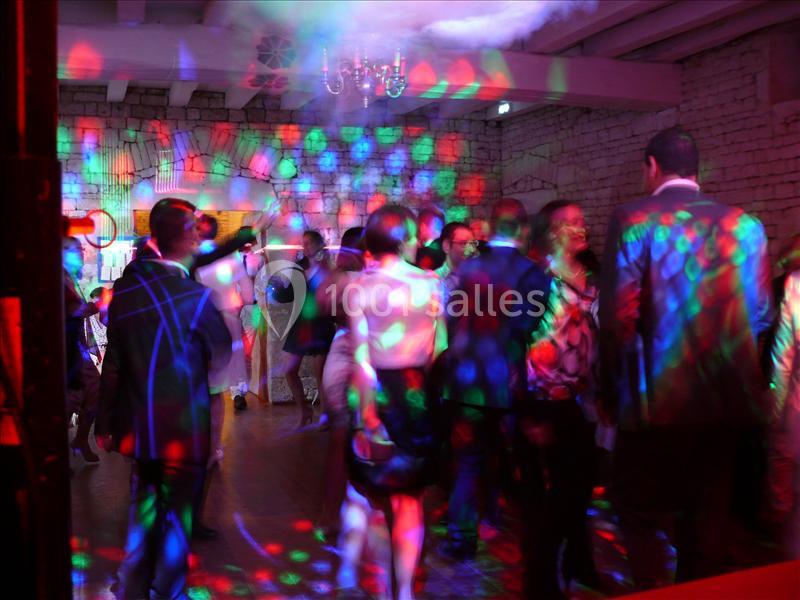 Soirée dansante Personnes dansant sous des lumières colorées dans une salle avec murs en pierre et plafond en poutres apparentes.