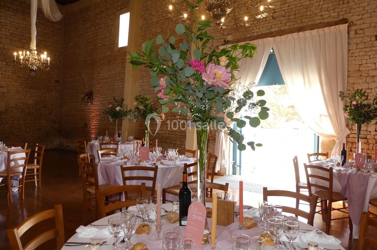 vases géants pour centre de table Salle de réception décorée avec des tables dressées, nappes roses, bouquets de fleurs et lumière naturelle entrant par une…