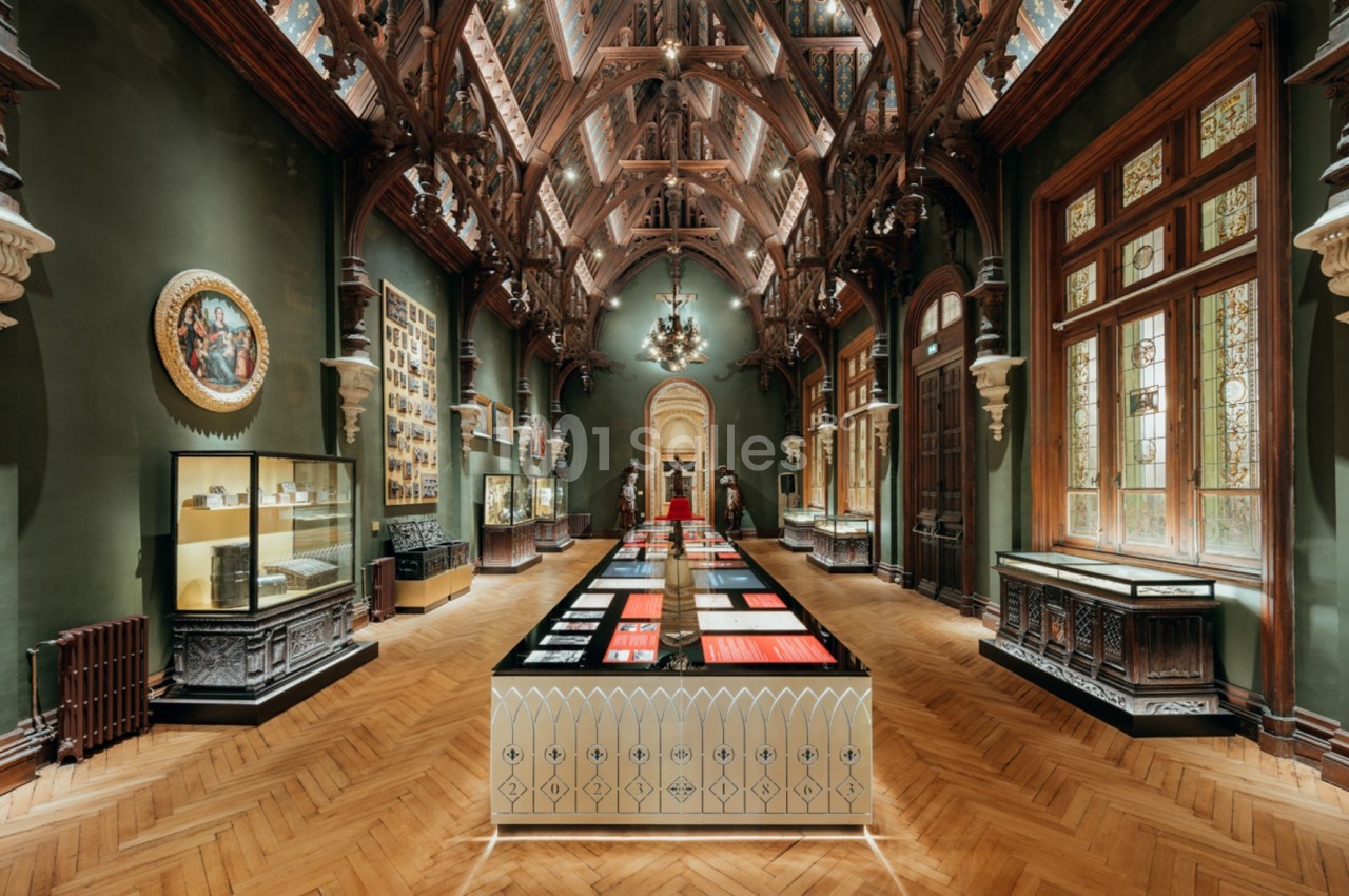 Salle d'exposition avec un plafond orné, des vitrines, des objets exposés et un parquet en bois.
