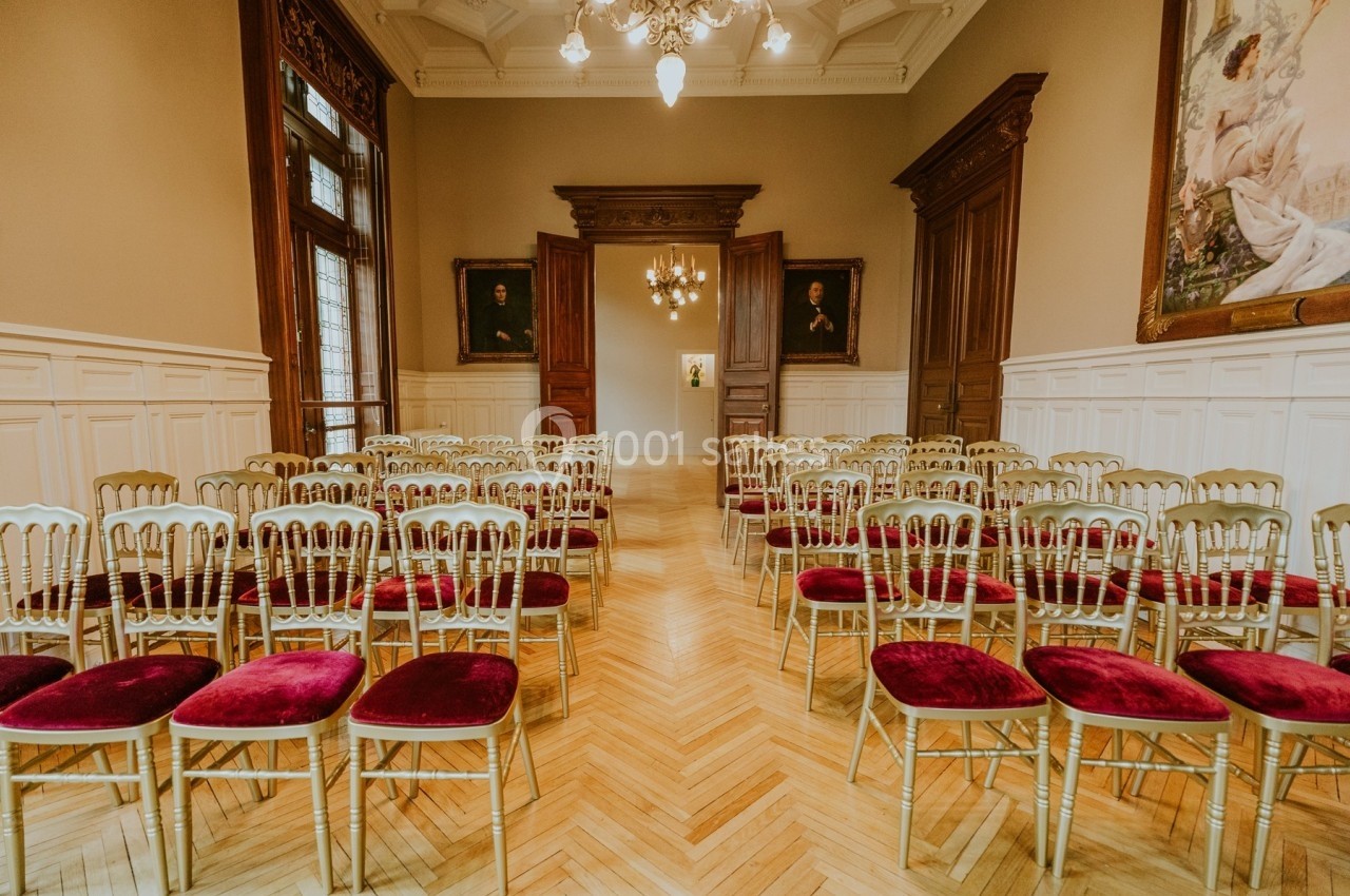 Rangées de chaises dorées avec assises rouges disposées dans une salle élégante au parquet clair et murs ornés.