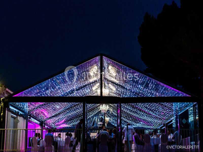 Structure transparente illuminée par des guirlandes lumineuses, abritant un événement nocturne avec des invités.