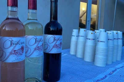 Miniature Location salle Ansouis (Vaucluse) - Le Grand Turcan #14 Salle avec un ancien pressoir en bois, des tonneaux, une table rouge avec bouteilles et des verres à vin.