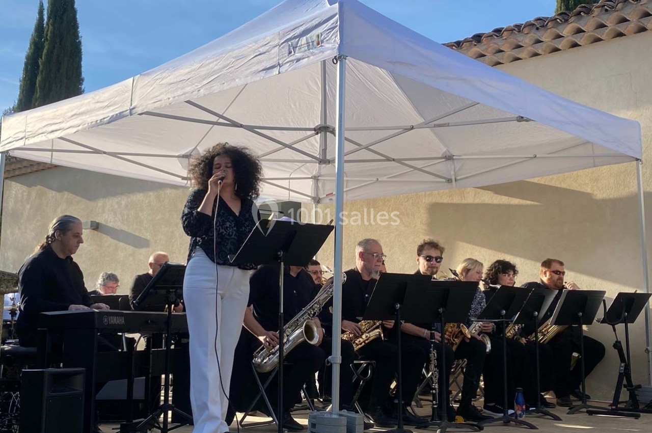 Location salle Ansouis (Vaucluse) - Le Grand Turcan #12 Chanteuse interprétant une chanson sur scène, accompagnée d'un orchestre sous une tente blanche en extérieur.