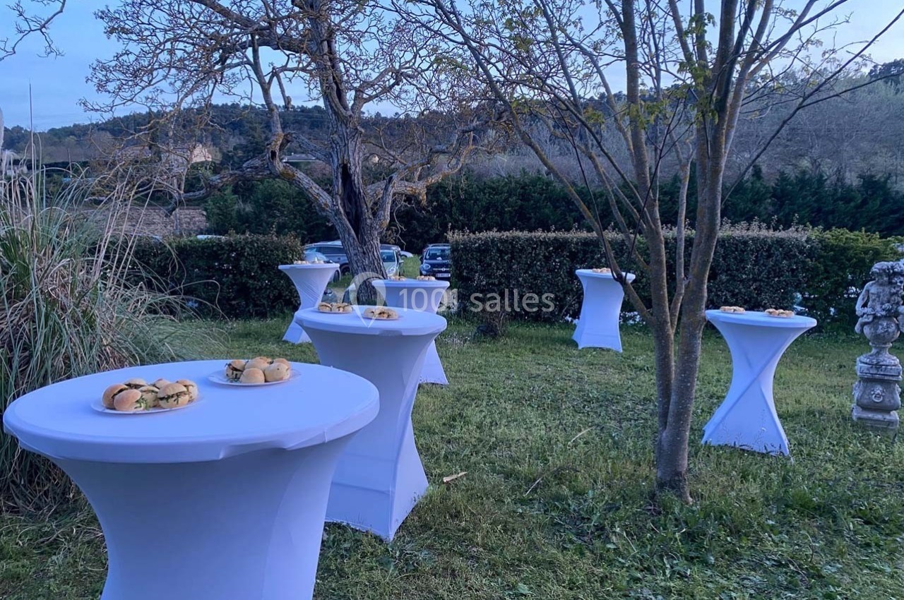 Location salle Ansouis (Vaucluse) - Le Grand Turcan #9 Tables hautes blanches dressées avec des plateaux de sandwichs dans un jardin au crépuscule.