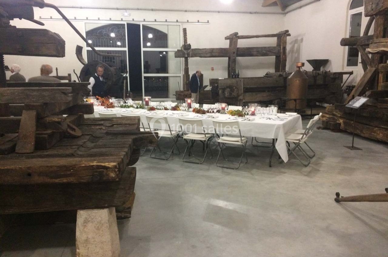 Location salle Ansouis (Vaucluse) - Le Grand Turcan #16 Salle avec des pressoirs anciens en bois, une longue table dressée pour un repas, et quelques personnes en arrière-plan.