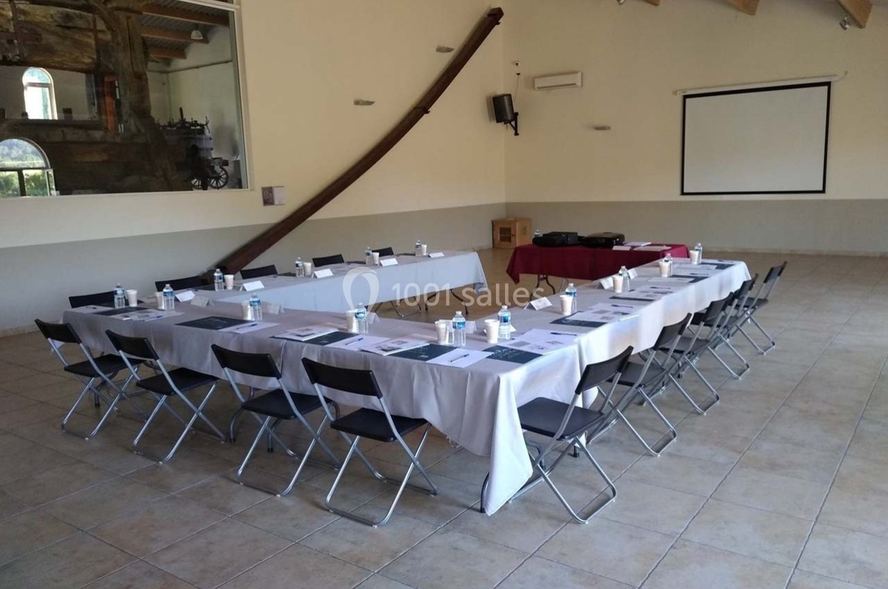Location salle Ansouis (Vaucluse) - Le Grand Turcan #15 Salle de réunion avec deux rangées de tables dressées, chaises pliantes, écran de projection et matériel de présentation.