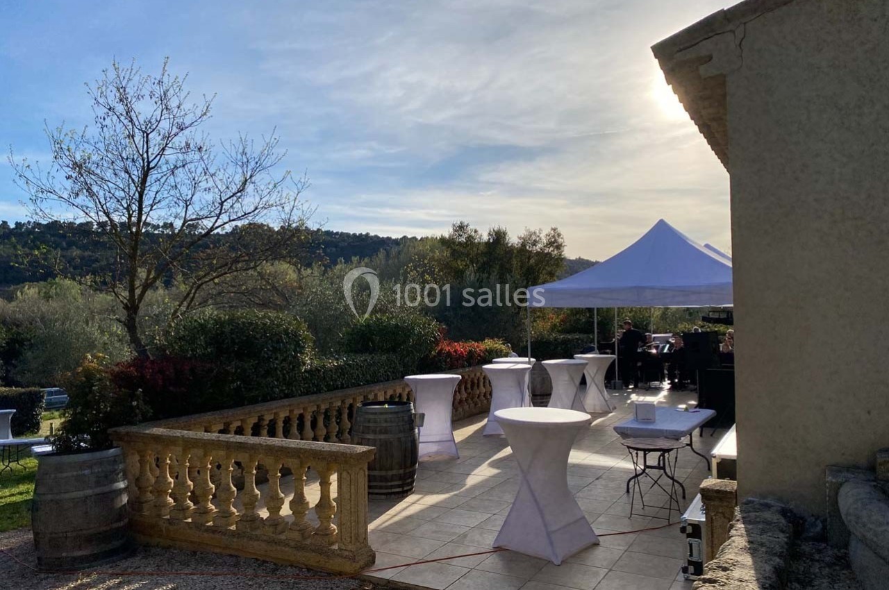 Location salle Ansouis (Vaucluse) - Le Grand Turcan #4 Terrasse ensoleillée avec tables hautes et tonnelle blanche, entourée de végétation et collines en arrière-plan.