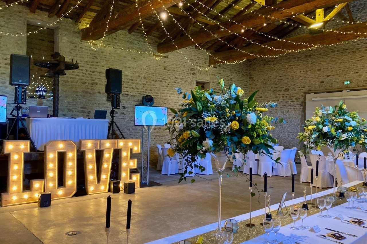 Salle de réception décorée pour un mariage avec guirlandes lumineuses, grandes compositions florales et lettres ’LOVE…