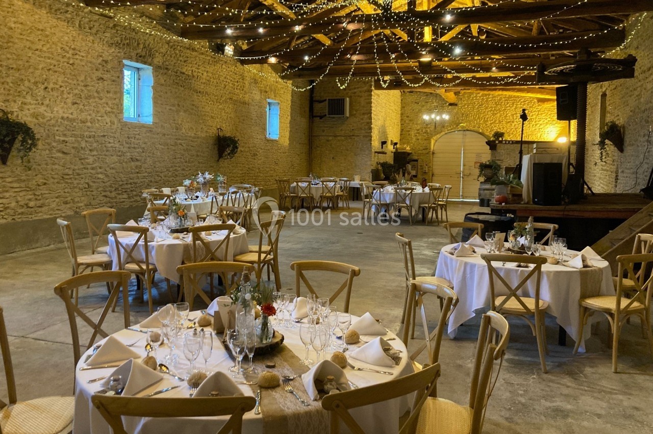 Salle de réception en pierre avec tables rondes dressées, décorations lumineuses suspendues et ambiance chaleureuse.