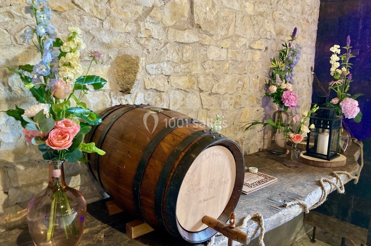 Baril en bois sur une table en pierre, entouré de fleurs colorées et de lanternes dans un décor rustique.