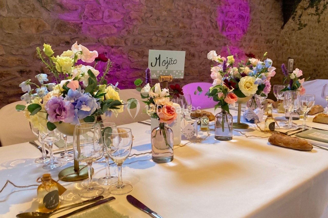 Table décorée pour un événement avec fleurs colorées, vaisselle élégante et pancarte ’Mojito’ sur fond de mur en pierre.