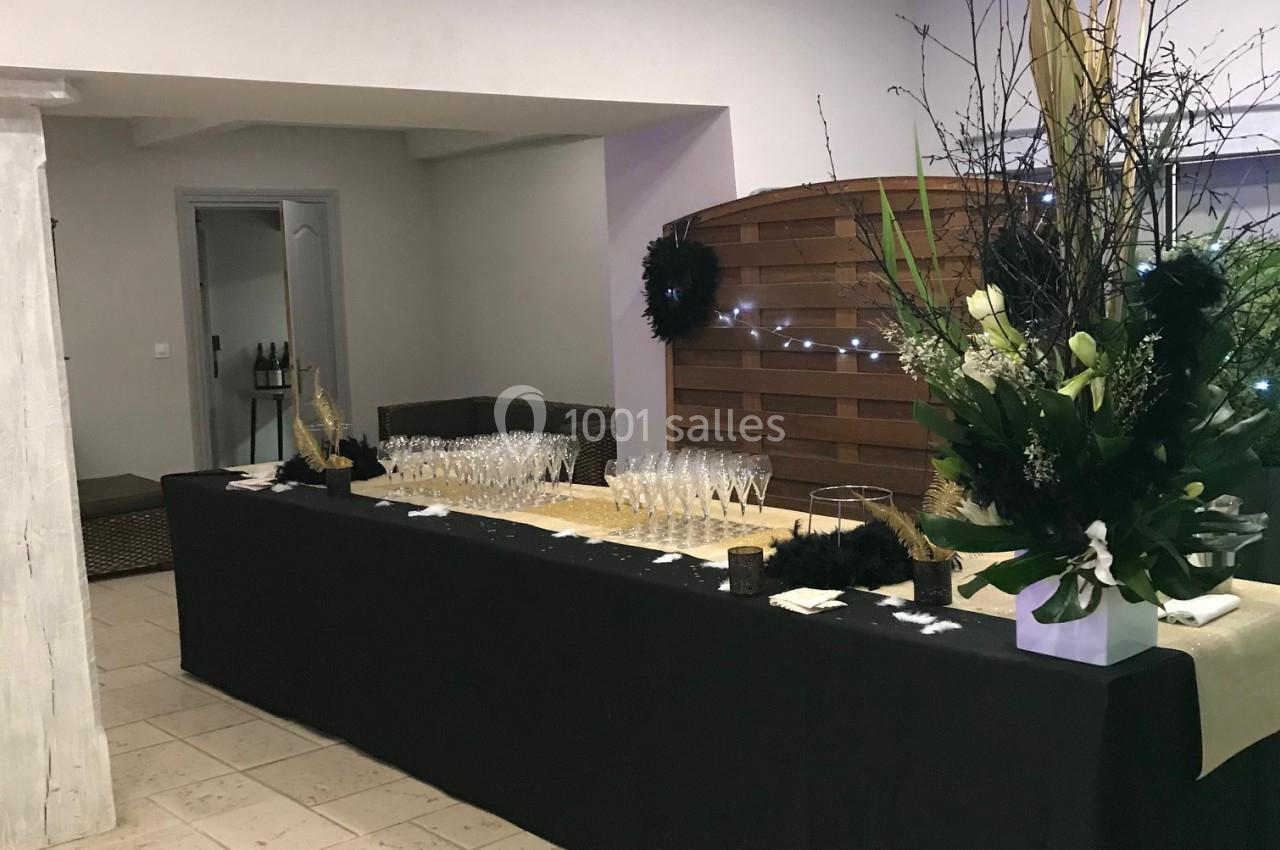 Table décorée avec une nappe noire, des verres à pied alignés et un grand bouquet floral dans une salle lumineuse.