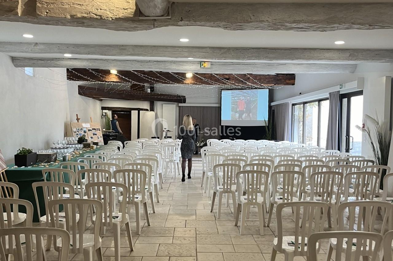 Salle de conférence lumineuse avec des rangées de chaises blanches, un écran de projection et une table de buffet.